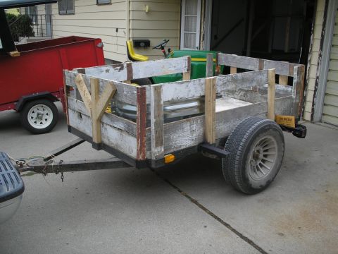 1990 Ford Bronco - A weathered wooden trailer is parked next to a red utility trailer.