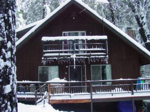 1986 Ford Bronco - A rustic cabin is blanketed in fresh snow, surrounded by snow-covered trees.