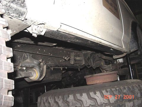 1990 Ford Bronco - The underside of a white 1990 Ford Bronco is visible, including its frame, suspension components, and a large tire.
