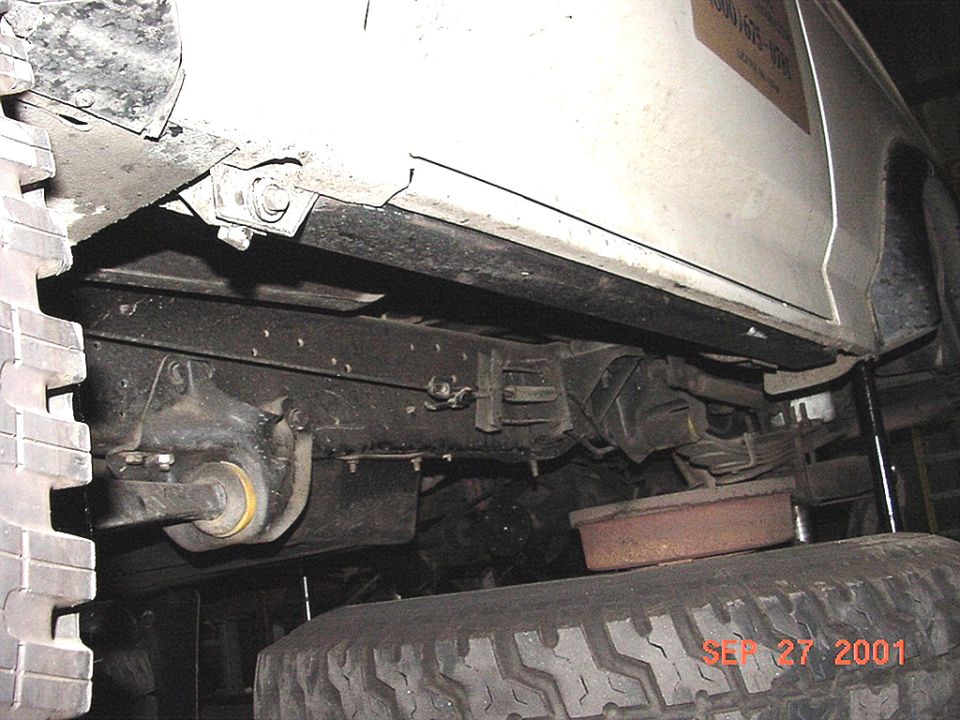 Underside of white 4x4 showing frame rail, rocker guard bracket, leaf spring and shock