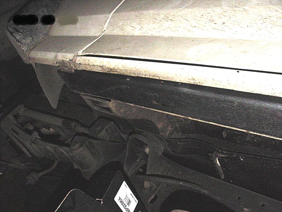 Black steel rocker guard bolted along the lower sill of a white truck body, viewed from below