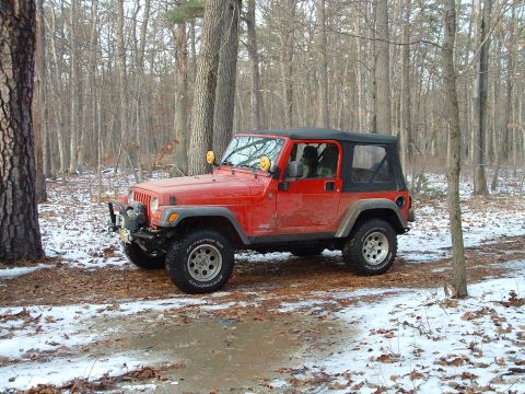 1978 Chevrolet C/K Pickup - A red Jeep Wrangler is seen in a wooded area with patches of snow on the ground.