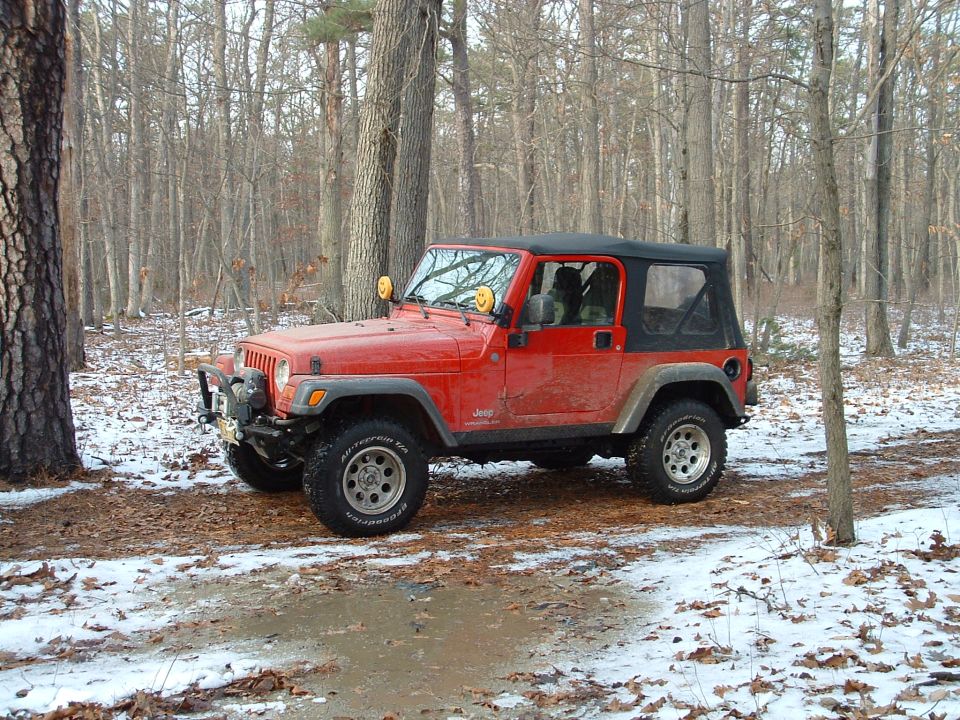 Red Jeep Wrangler with winch bumper and soft top on a snowy wooded trail