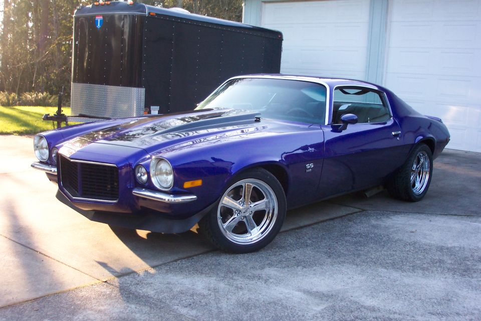 Purple 1970 Chevrolet Camaro SS with chrome wheels parked in front of a garage and trailer