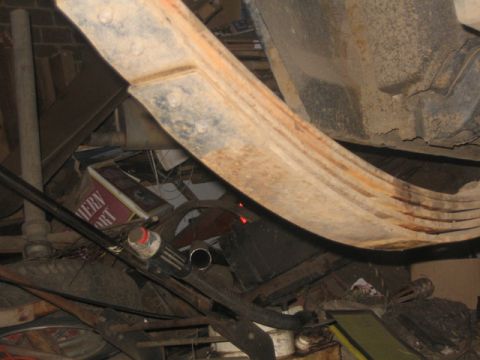 1981 Ford Bronco - The photo shows the undercarriage of a vehicle, focusing on a leaf spring and exhaust system, with other items stored nearby.
