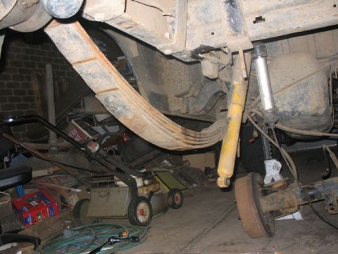 1981 Ford Bronco - Close-up view of the rear suspension components, including leaf springs and a shock absorber, in a cluttered garage setting.