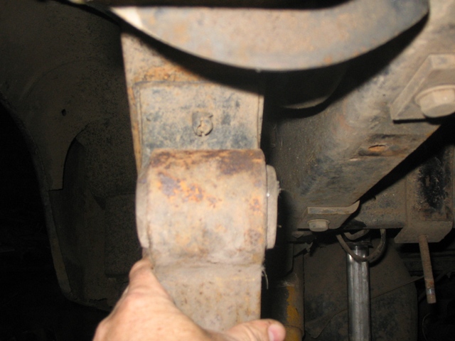 Rusty leaf spring assembly with a hand pointing to it, showing suspension parts