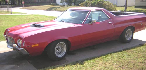 Red Ford Ranchero with hood scoop and silver wheels parked on a driveway, front three-quarter view