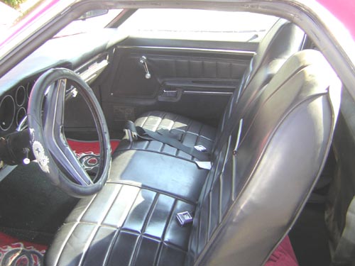 car interior with black seats, steering wheel, and door panel. Red carpet visible