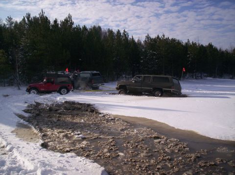 1996 Ford Bronco - Multiple SUVs are stuck in a snowy and muddy terrain, with one vehicle attempting to tow another out.
