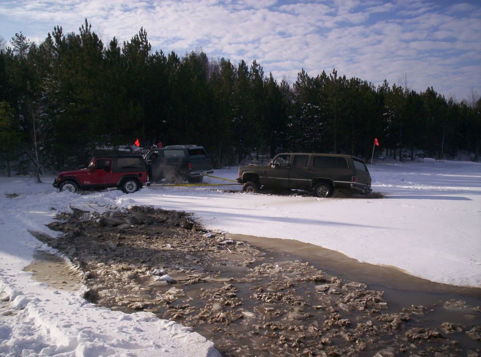 Three SUVs stuck in snow and mud, one being towed by another