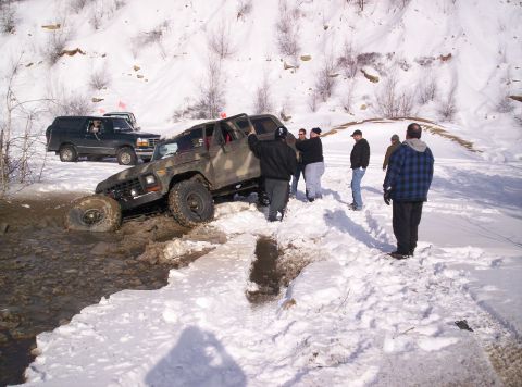 1996 Ford Bronco - Two off-road vehicles are in a snowy landscape, with one stuck in mud and several people observing.
