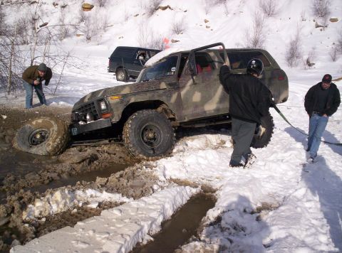 1996 Ford Bronco - A camouflage SUV is stuck in mud and snow, with people attempting to free it.