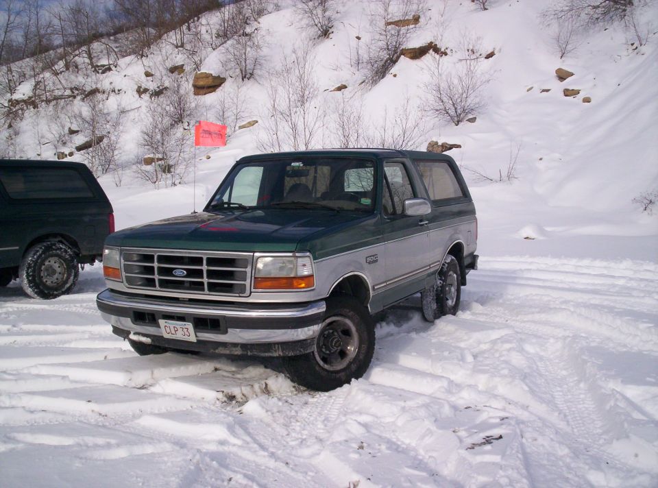 Green and silver Ford Bronco in snow, another dark SUV behind it