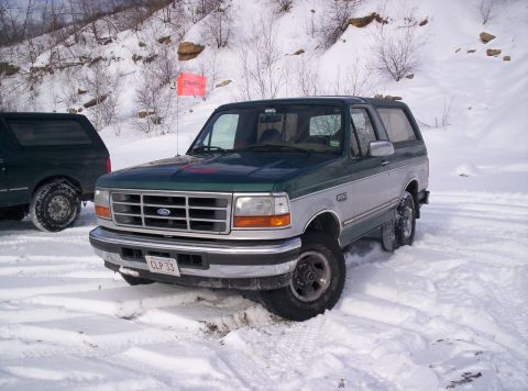 1996 Ford Bronco - A two-tone green and silver 1996 Ford Bronco navigates a snowy terrain, with another Bronco visible in the background.