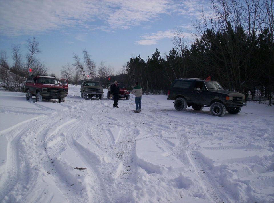 Black Ford Bronco in snow with other vehicles and people around