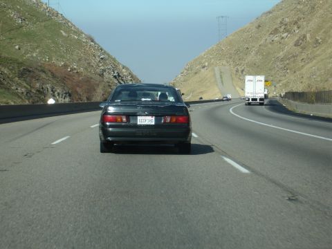 1995 Ford Taurus - A black 1995 Ford Taurus is seen from behind on a highway, with a semi-truck in the distance.