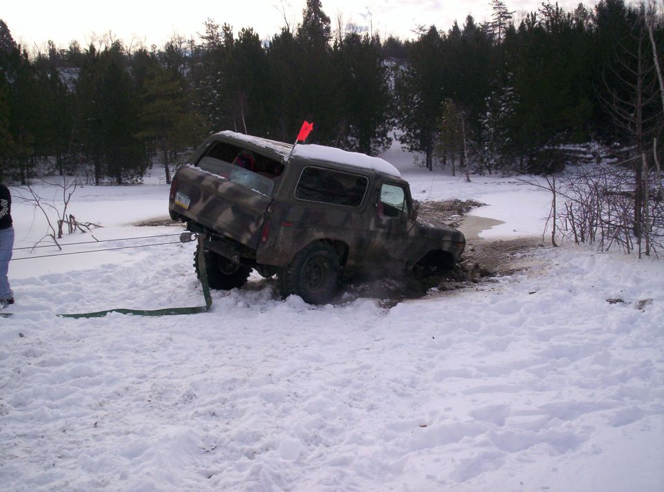 Camouflaged SUV stuck in mud and snow, being pulled by a strap