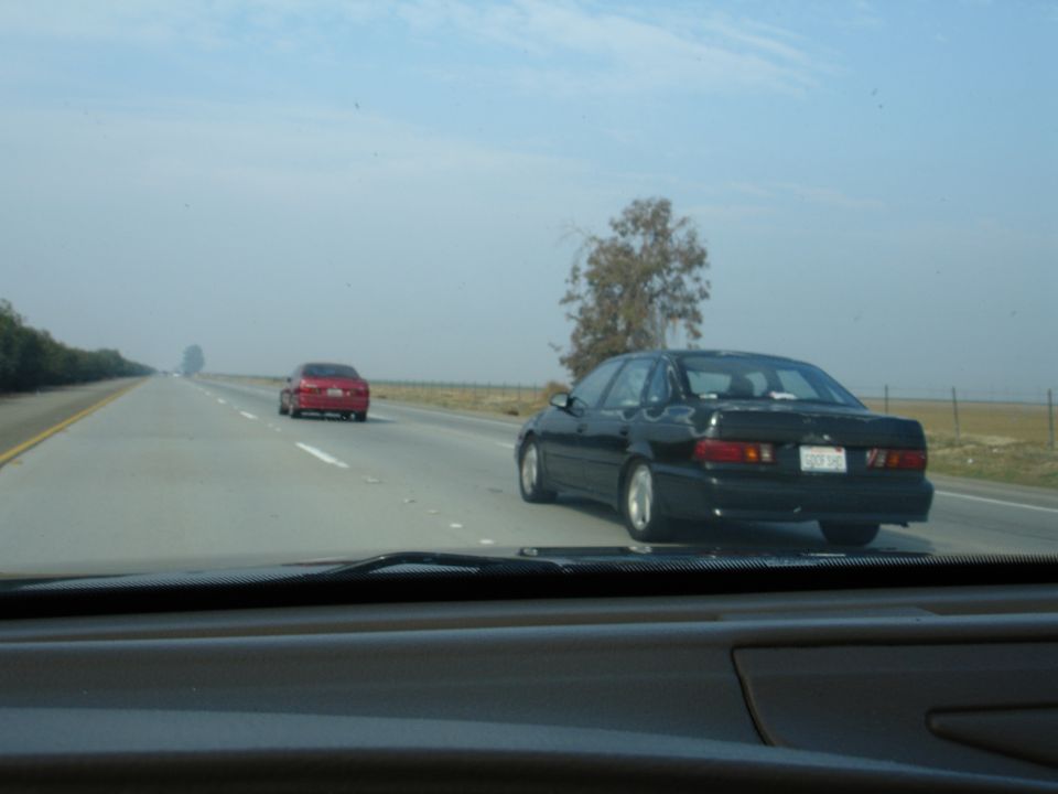 Black 1995 Ford Taurus sedan from rear, driving on highway with a red car ahead