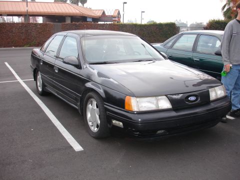 1995 Ford Taurus - A black sedan is parked in a lot, with another car visible behind it.