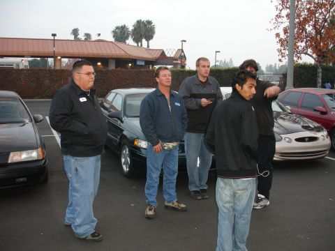 1995 Ford Taurus - Several men gather in a parking lot, with multiple vehicles in the background.