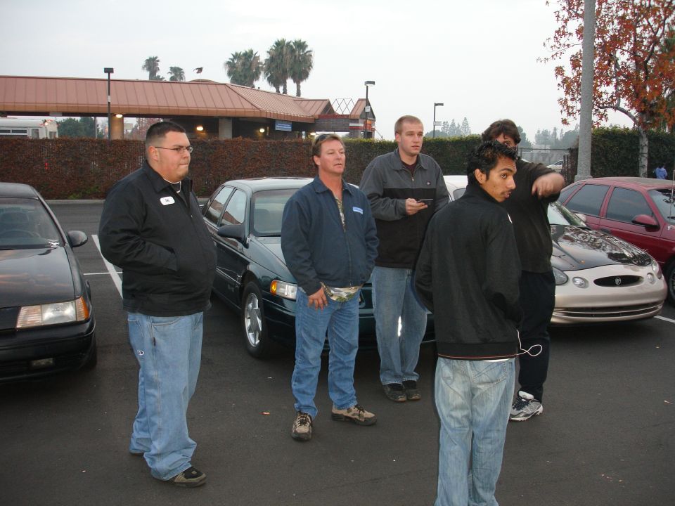 Group of men standing in a parking lot with several cars visible