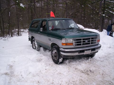 1996 Ford Bronco - This Ford Bronco is navigating a snowy path with trees in the background.