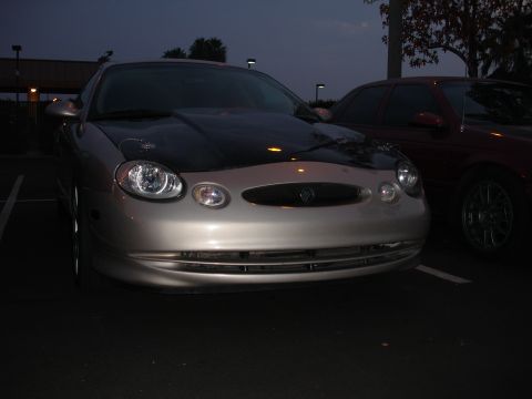 1995 Ford Taurus - A silver Mercury Sable with a black hood is parked next to another car at dusk.