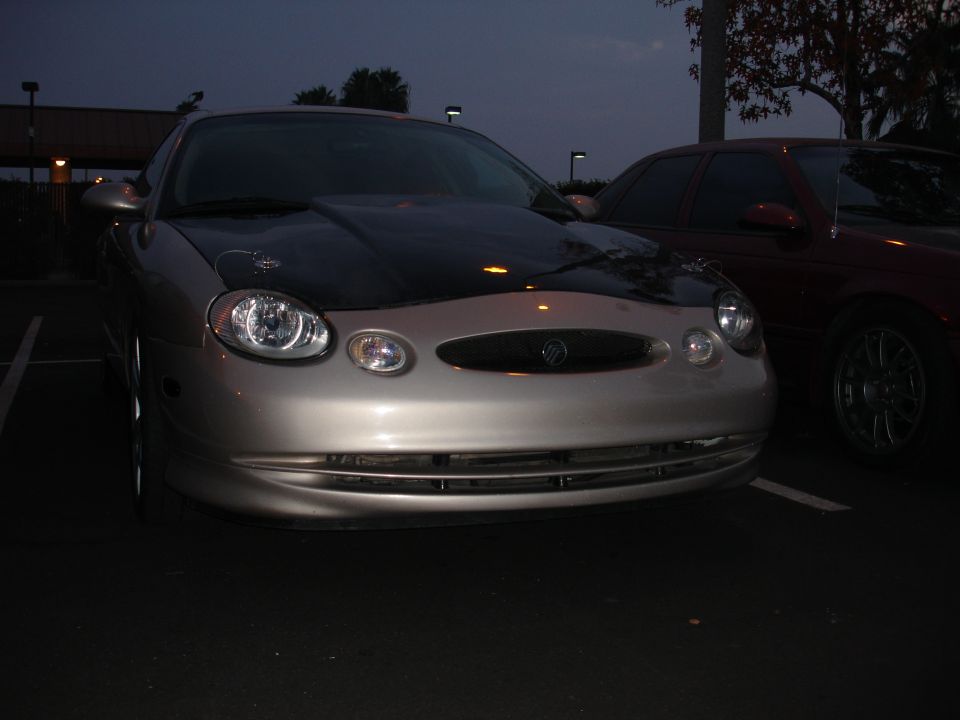 Silver Mercury Sable with a black hood, parked at dusk