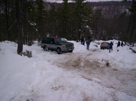 1996 Ford Bronco - Two SUVs navigate a snow-covered path in a wooded area.