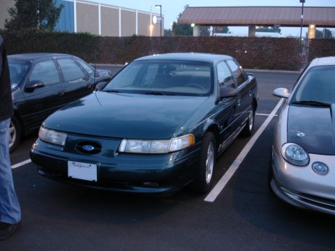 1995 Ford Taurus - A dark green sedan is parked in a lot, with other vehicles visible on either side.