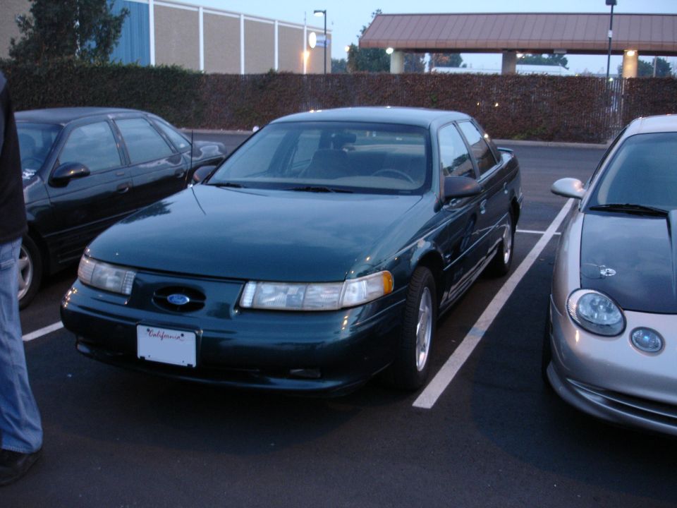 Dark green Ford Taurus parked in a lot. Another car is to its left and a silver car is to its right