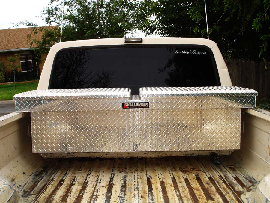 Rear view of a pickup truck bed with two diamond plate toolboxes. A sticker on the rear window reads 'San Angelo Dragway'