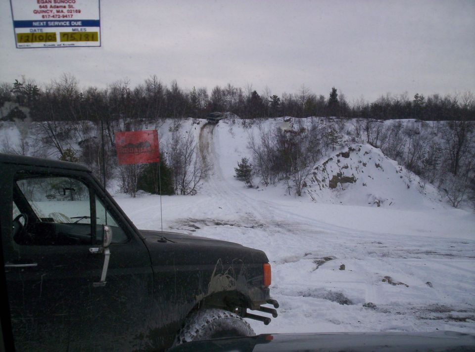 Dark off-road vehicle in snowy terrain with a dirt track going up a hill in the background