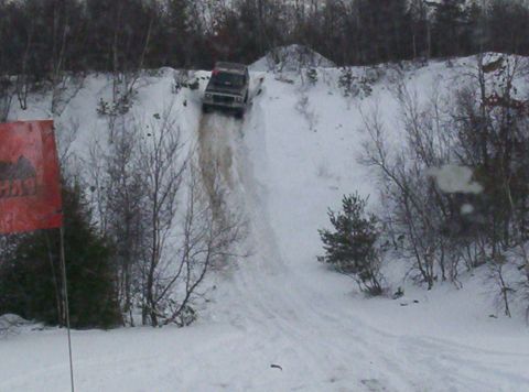 1996 Ford Bronco - A 1996 Ford Bronco navigates a challenging snowy incline, kicking up snow as it descends.