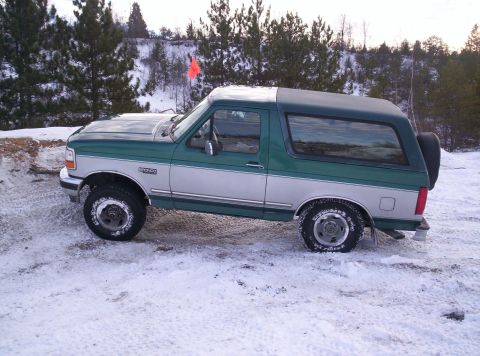 1996 Ford Bronco - This two-tone Ford Bronco is parked in a snowy outdoor setting with trees in the background.