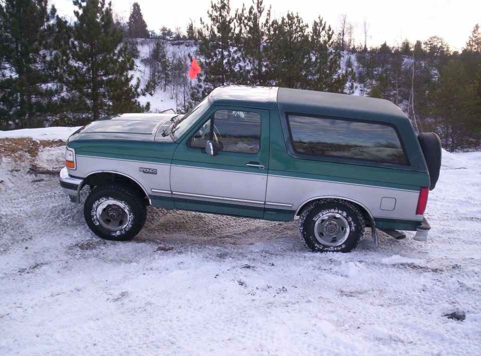 Green and silver Ford Bronco parked in snow. Bronco badge visible on the side