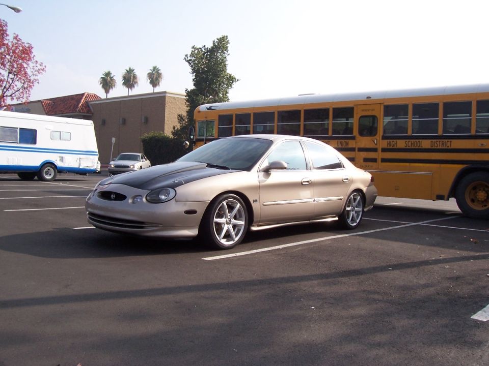 1998 Mercury Sable, tan sedan with black hood, parked next to a school bus