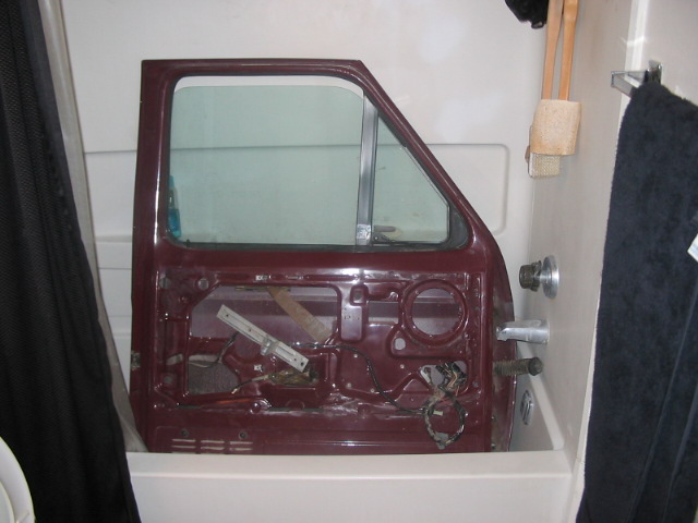 Maroon car door with window removed, showing interior mechanisms, resting in a bathtub
