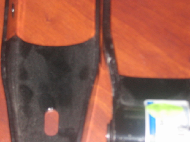 Two black metal automotive parts on a wood-grain surface. One part has a red oval sticker