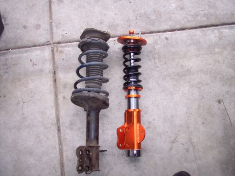 1995 Ford Probe - Comparison of an old suspension strut next to a new, orange adjustable coilover suspension part.