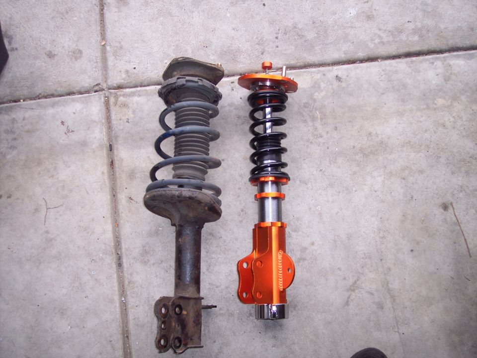 Two suspension struts, one old and rusty, the other new and orange with adjustable coilovers