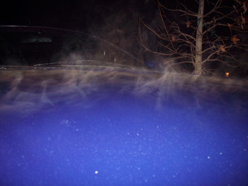 Blue car hood with steam rising off it at night