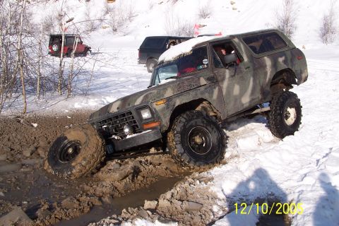 1979 Ford Bronco - A camouflaged Ford Bronco navigates a challenging muddy and snowy terrain with another vehicle visible in the background.