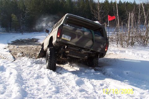 1979 Ford Bronco - A 1979 Ford Bronco with camouflage paint is stuck in the snow, its rear end visible with a red flag mounted on the antenna.