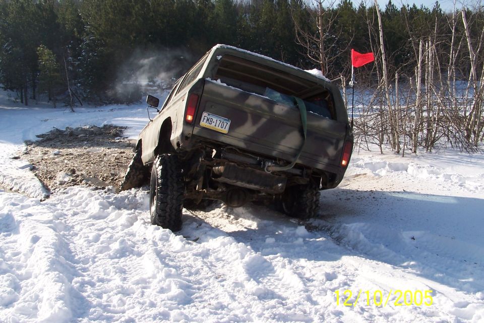 Green camo lifted 4x4 climbing a snowy mud hole, rear axle exposed