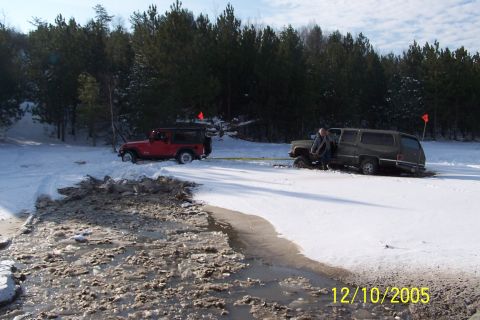 1979 Ford Bronco - Two off-road vehicles are stuck in a snowy and icy terrain, with one vehicle appearing to be pulled by the other.