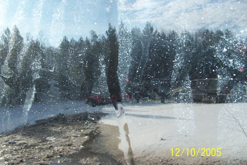 Red SUV partially visible through a snow-covered windshield with trees and other vehicles in the background