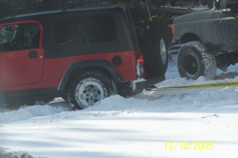 1979 Ford Bronco - A red Jeep Wrangler is stuck in deep snow, with another vehicle partially visible behind it.