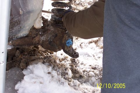 1979 Ford Bronco - A person works on a muddy and snow-covered vehicle suspension part, likely during a repair.